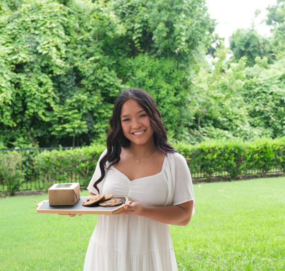 Britney smiling in the backyard, holding a tray of fresh chocolate chip cookies and a cookie box