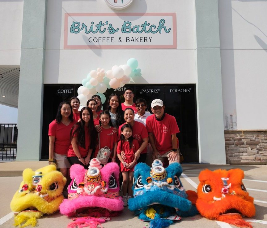 A group in red Brit’s Batch shirts with four lion dance heads in front of the Brit’s Batch Coffee & Bakery storefront on Texas 249